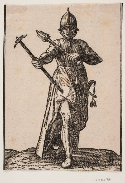 Stående hjelmklædt soldat, frontalt set; i h. hånd en stridshammer, i v. hånd en stridskølle, bageste ben og fod forvredet i forhold til forreste; ved v. side et sværd